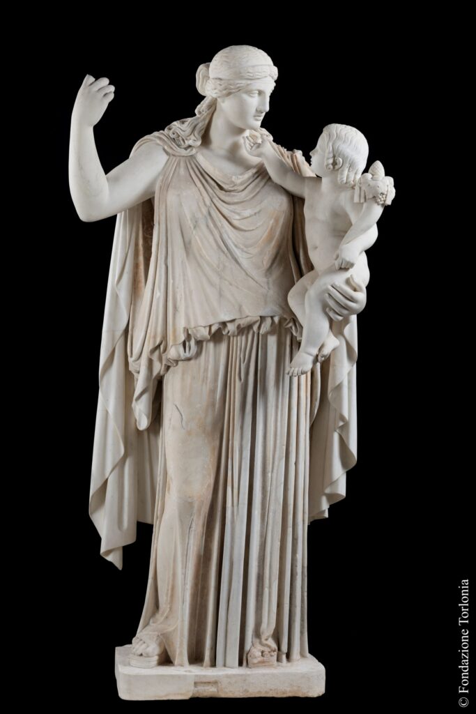 Sculpture of woman holding infant on left hip while raising right hand to head height. The infant is reaching towards the woman's face.